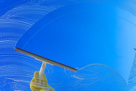 Window cleaner using a squeegee or wiper to wash a window glass. Hand in yellow glove hold cleaning...