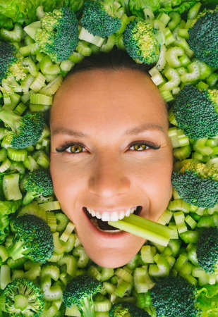 Smiling woman face on a fresh green broccoli and celery background. Woman with vegetables. Vegan detox diet. Healthy eatingの写真素材