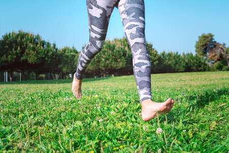 Sporty barefoot woman running on the green grass. Young female legs running barefoot