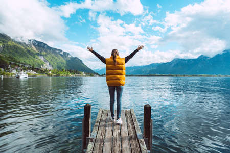 Young woman traveler with open arms standing on wooden bridge and enjoying great view on Geneva lake in Switzerlandの写真素材