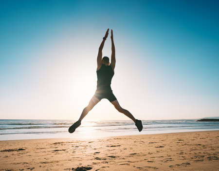 Jumping man. Young fitness man doing jumping jacks or star jump exercise on the beachの写真素材