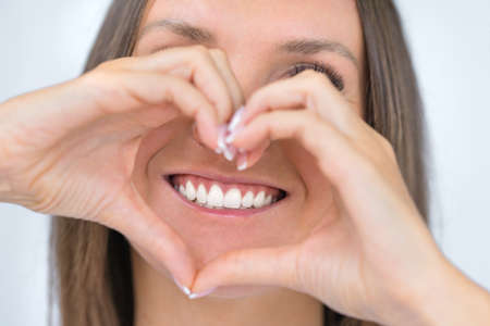 Teeth care. Woman with beautiful smile with strong white teeth. Dental care. Woman holding heart shaped hands near perfect healthy teeth. Stomatology or dentistry conceptの写真素材