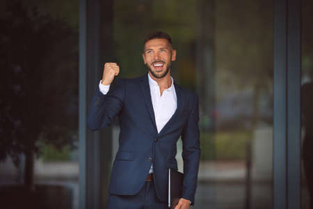 Happy businessman celebrating success and showing winner gesture. Young smiling office worker...