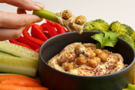 Closeup of woman hand holding celery stick with chickpeas hummus. Tasty hummus with vegetables and smoked paprikaの写真素材