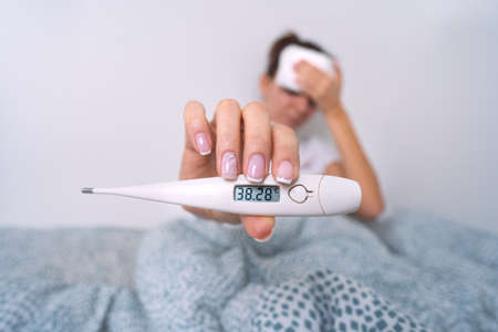 Sick woman with a high fever showing medical thermometer with temperature 38,2. Woman measuring body temperatureの写真素材
