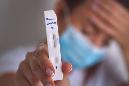 Sick infected woman showing rapid covid antigen test or express covid test with positive covid-19...