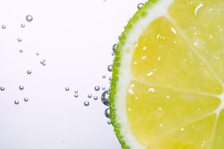 Macro photo of lime slice In water with bubbles isolated on white background. Freshness and healthy...