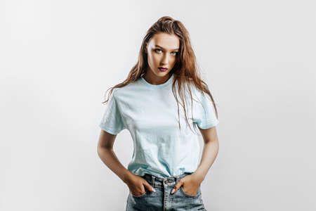 Beautiful young brunette girl with green eyes with long hair with fashion makeup with purple lips on an isolated gray background. The woman seriously looking at the camera. Kind cute modelの写真素材
