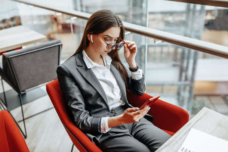 Business woman in glasses at the workplace uses the phone and sits at the table. Manager in the...