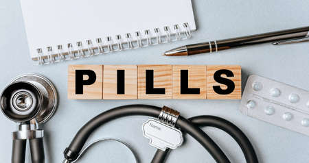 Wooden block form the word PILLS with stethoscope, pills, notepad, pen on the doctor's desktop. Medical concept.の写真素材