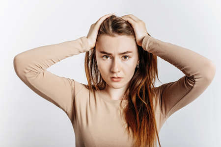 Beautiful young brunette girl in horror holding her head on an isolated white background. The woman is shocked by the bad news. Advertising spaceの写真素材