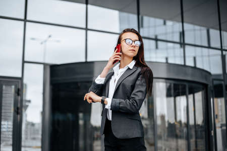 A business woman checks the time and talking on the phone in the city during a working day waiting for a meeting. Discipline and timing. An employee goes towards a corporate meeting.の写真素材