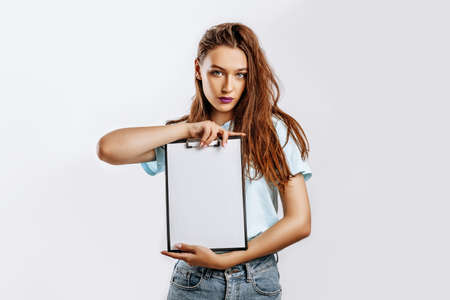 Young beautiful girl holding a board of papers on an isolated gray background. Business concept. A woman with purple lips and long dark hair. Place for advertising.の写真素材