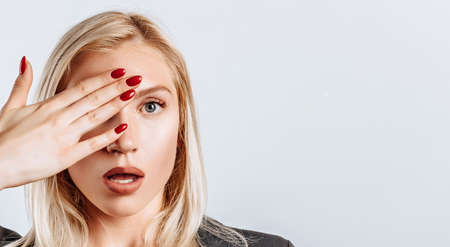 The blonde girl is surprised badly covers half of her face with her hand. The woman remembered, learned and understood important information about the business. Isolated background for advertising.の写真素材