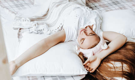 A sleepy brunette girl lies in bed with a blindfold waking up in the morning. Cozy home morning in cute pajamas. Have a good time, relax and dream. Healthy sleep.の写真素材