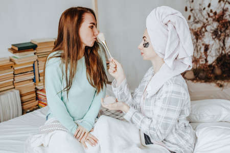 Two girls make masks and patches for the beauty of face and hair. Women take care of youthful skin. Girlfriends laugh, make faces and do beauty treatments at home with towels on their heads.の写真素材