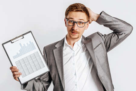 Young handsome brunet man in glasses in a suit is unhappy with business documents and charts on a white isolated backgroundの写真素材