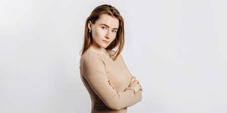 Beautiful young girl smiling and posing looking at the camera on a white isolated background. Positive brunette woman in a beige jumper. Kind look.の写真素材