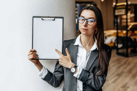 The woman shows information on the tablet. Place for advertising. Business concept. The girl in glasses holds the documents and explains the information. White blank sheet of paper.の写真素材