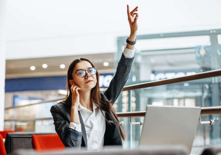 A woman calls a colleague, waves her hand for a meeting. Girl works on a laptop in the workplace. Successful business woman creates a startup and makes decisions.の写真素材