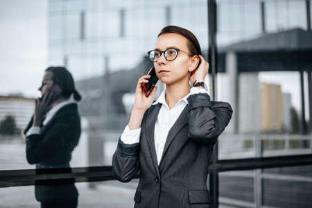 A business woman talking on the phone in the city during a working day waiting for a meeting. Discipline and timing. An employee goes towards a corporate meeting.の写真素材