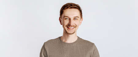 Young handsome man smiling with a brunet beard. Student, worker, businessman posing for photo isolated on gray background. Place for advertising.の写真素材