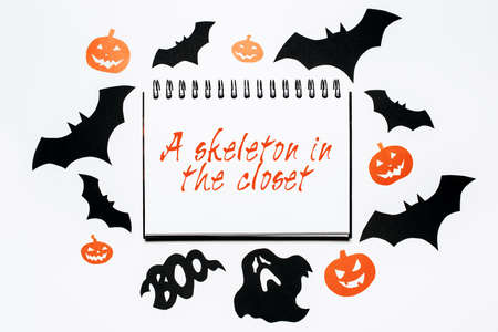 Happy halloween holiday concept. Notepad with text A skeleton in the closet on white background with bats, pumpkins and ghostsの写真素材