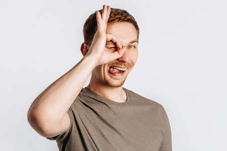 Young handsome brunet man with beard says ok and winks on white isolated background