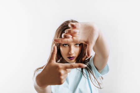 Beautiful young girl makes a frame with her hands on an isolated gray background. The woman with fashion make-up with purple lips seriously looking at the camera. Place for advertising.の写真素材