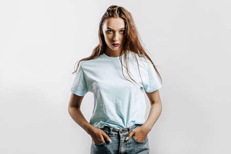 Beautiful young brunette girl with green eyes with long hair with fashion makeup with purple lips on an isolated gray background. The woman frowning and seriously looking at the camera. Evil modelの写真素材