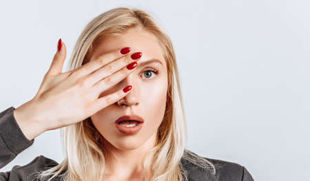 The blonde girl is surprised badly covers half of her face with her hand. The woman remembered, learned and understood important information about the business. Isolated background for advertising.の写真素材