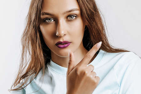 Young beautiful girl pointing finger to the side at on a white isolated background. A woman points to an idea, a place for advertising. Serious girl with fashion make-up with purple lips.の写真素材