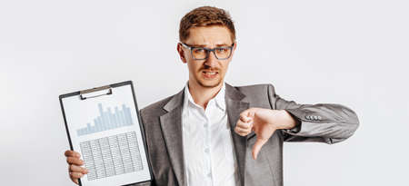 Young handsome brunet man in glasses in a suit is unhappy with business documents and charts on a white isolated backgroundの写真素材