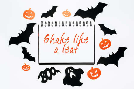 Happy halloween holiday concept. Notepad with text Shake like a leaf on white background with bats, pumpkins and ghostsの写真素材