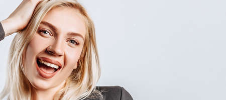 Hey smile at you. The blonde girl is happy and holds her hand to her head. A beautiful woman is pleased with an excellent business proposal. Nose piercing, rhinestone on the tooth. Isolated backgroundの写真素材
