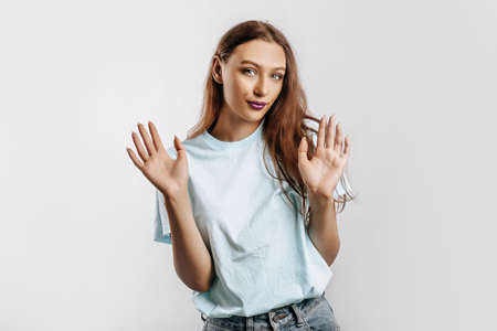 Stop. The woman raises her hands to the camera. The model feels confused and does not know what to choose. Beautiful sweet brunette girl with fashion makeup purple lips on an isolated gray backgroundの写真素材