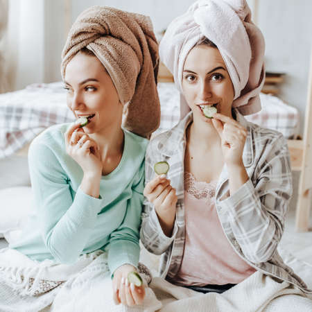Two girls make homemade face and hair beauty masks. Cucumbers for the freshness of the skin around the eyes. Women take care of youthful skinの写真素材