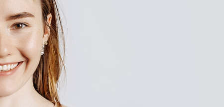 Young beautiful girl smiles on a white isolated background. Half face. A woman points to an idea, a place for advertising. Positive brunette in a beige jumper.の写真素材