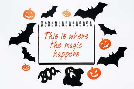 Happy halloween holiday concept. Notepad with text This is where the magic happens on white background with bats, pumpkins and ghostsの写真素材