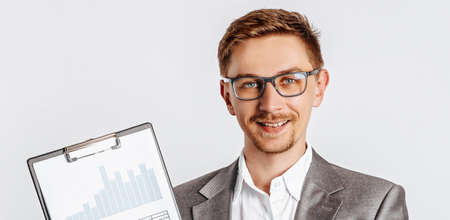 Young handsome brunette man in glasses in suit with business documents and charts on white isolated backgroundの写真素材