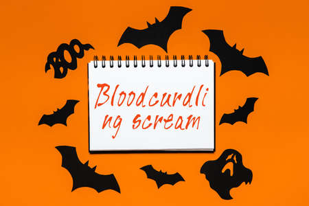 Happy halloween holiday concept. Notepad with text Bloodcurdling scream on white and orange background with bats, pumpkins and ghostsの写真素材