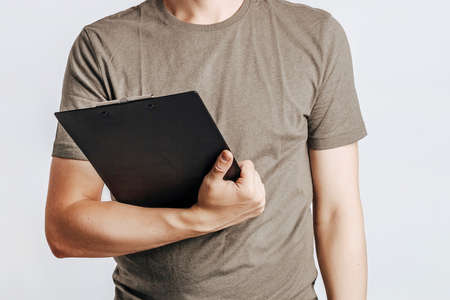 Young handsome man holding folder for papers with documents, student, worker looks data information, posing for photo isolated on gray background. Place for advertising.の写真素材