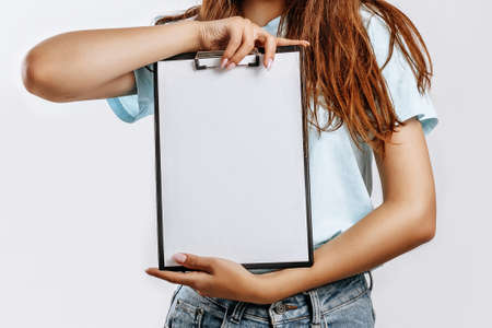 Young beautiful girl holding a board of papers on an isolated gray background. Business concept. A...