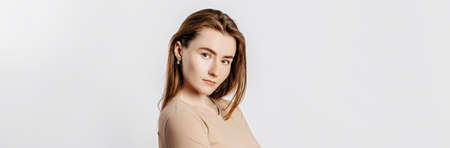 Beautiful young girl smiling and posing looking at the camera on a white isolated background. Positive brunette woman in a beige jumper. Kind look.の写真素材