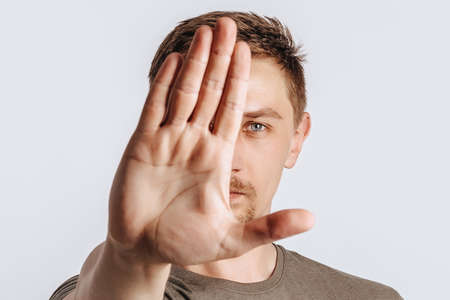 Young handsome brunette man with beard stretched out his hand forward and says STOP on white isolated backgroundの写真素材