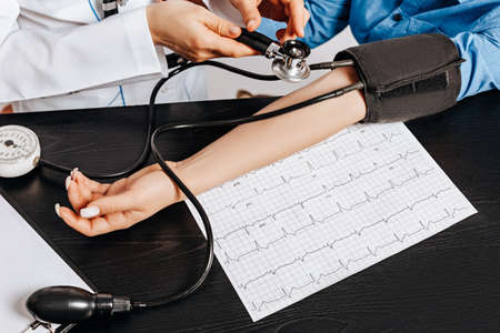 Doctor measures blood pressure with a tonometer to a woman patient at a medical appointment in a...