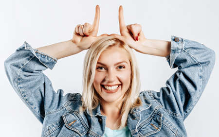 Beautiful young cute girl smiling fooling around and making horns gesture on gray isolated backgroundの写真素材