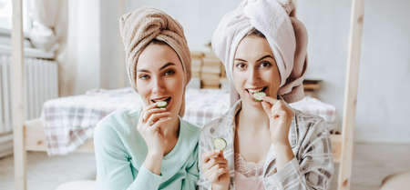 Two girls make homemade face and hair beauty masks. Cucumbers for the freshness of the skin around the eyes. Women take care of youthful skinの写真素材