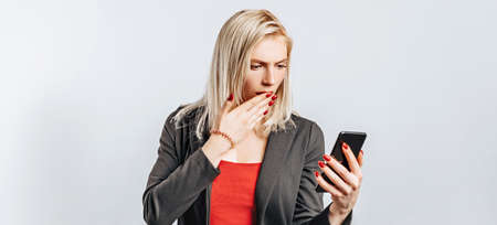 Beautiful young girl unhappy and holding phone on gray isolated backgroundの写真素材