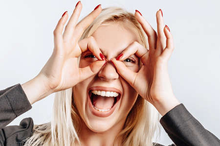 Beautiful young cute girl smiling fooling around and doing ok eye gesture on gray isolated...